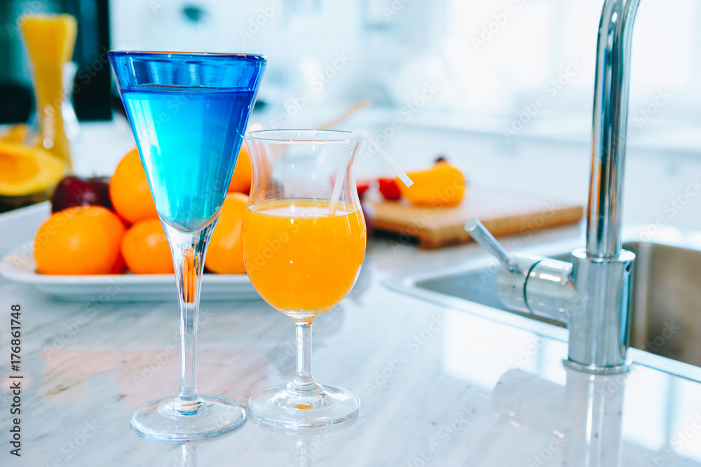 一杯橙汁和一杯水放在桌子上的一盘水果旁边，食物在