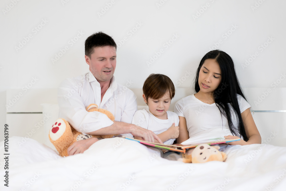 亚洲男孩与父亲和母亲一起在卧室的床上看书。幸福的家庭理念