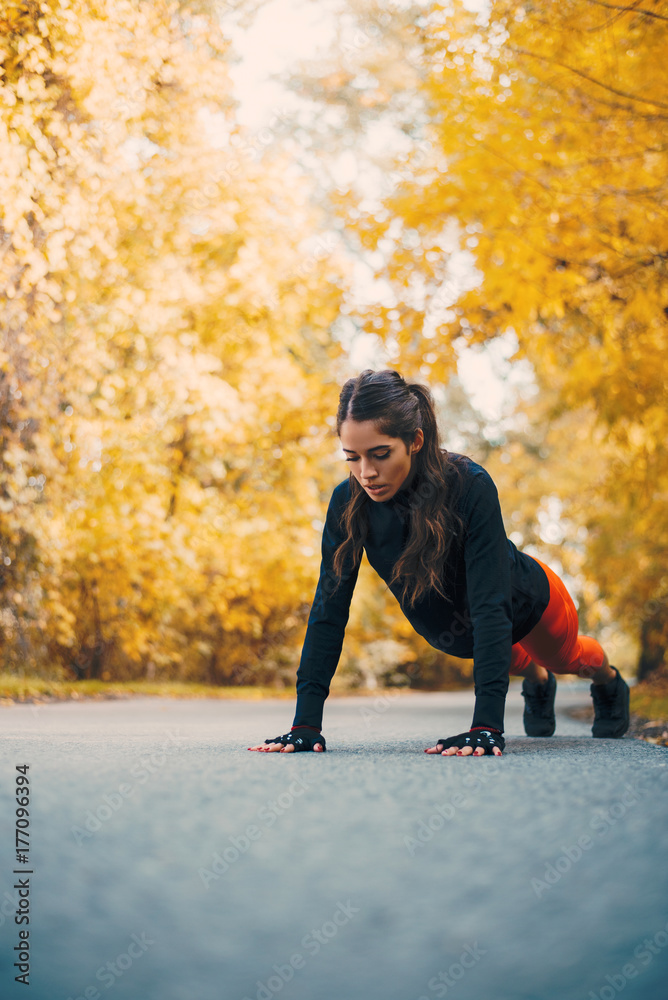 健身女士在秋季公园做俯卧撑。
