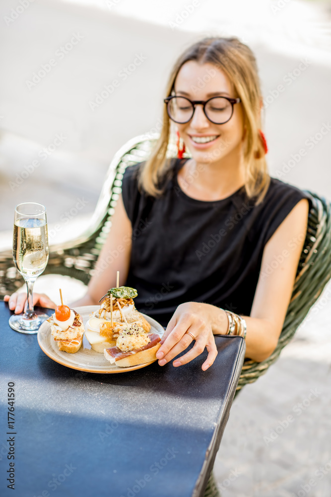 Young woman enjoying tasty appetizer with pinchos, traditional spanish snack, with glass of wine sit