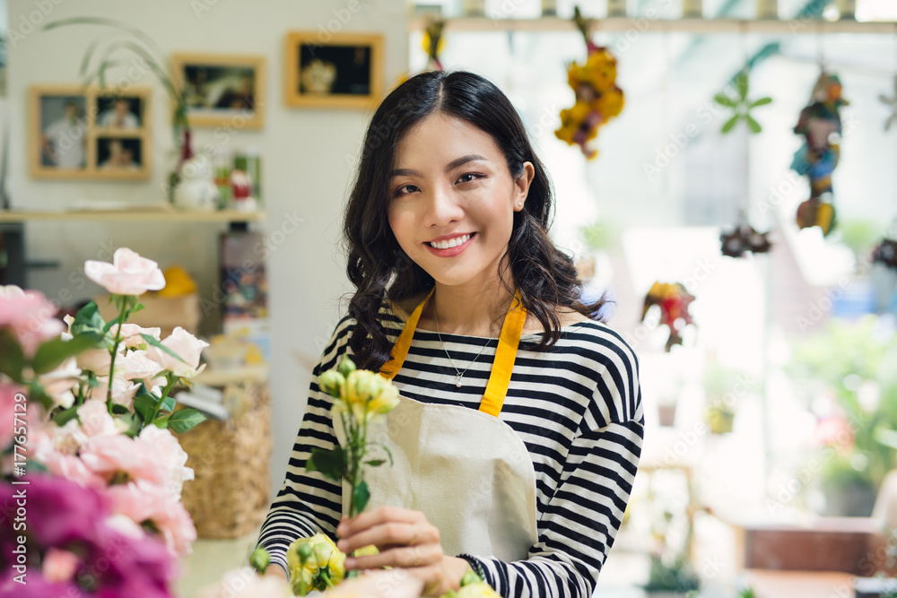 Young beautiful asian girl florist taking care of flowers at workplace.