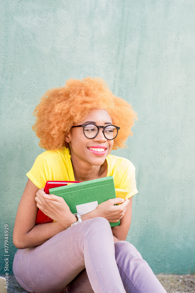 一位美丽的非洲学生的肖像，绿色墙壁背景上有五颜六色的书