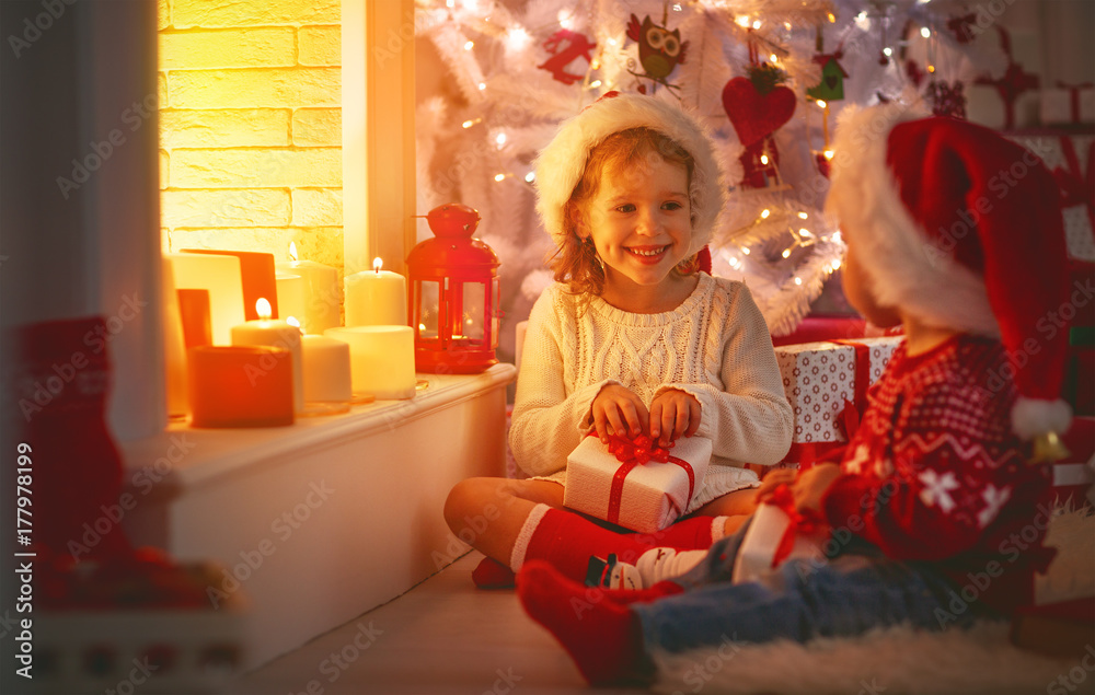 快乐的孩子们在圣诞树和壁炉旁拿着圣诞礼物。