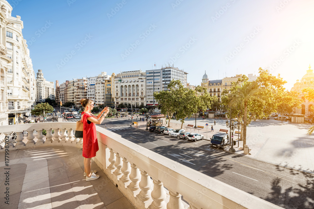 Young woman tourist in red dress photographing Ayuntamiento square from the terrace of city hall bui