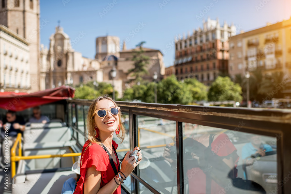 穿着红色连衣裙的年轻快乐女性游客在巴伦西亚市的开放式旅游巴士上游览，