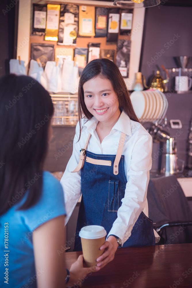 美丽的亚洲咖啡师将咖啡杯递给顾客，并在咖啡馆微笑