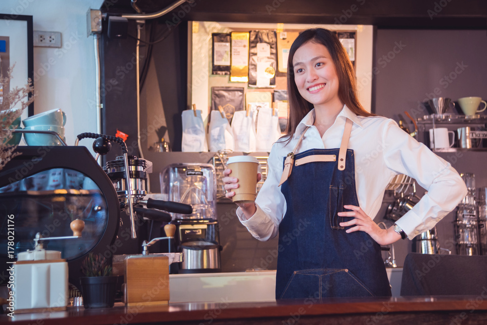 美丽的亚洲咖啡师拿着咖啡杯在咖啡馆微笑
