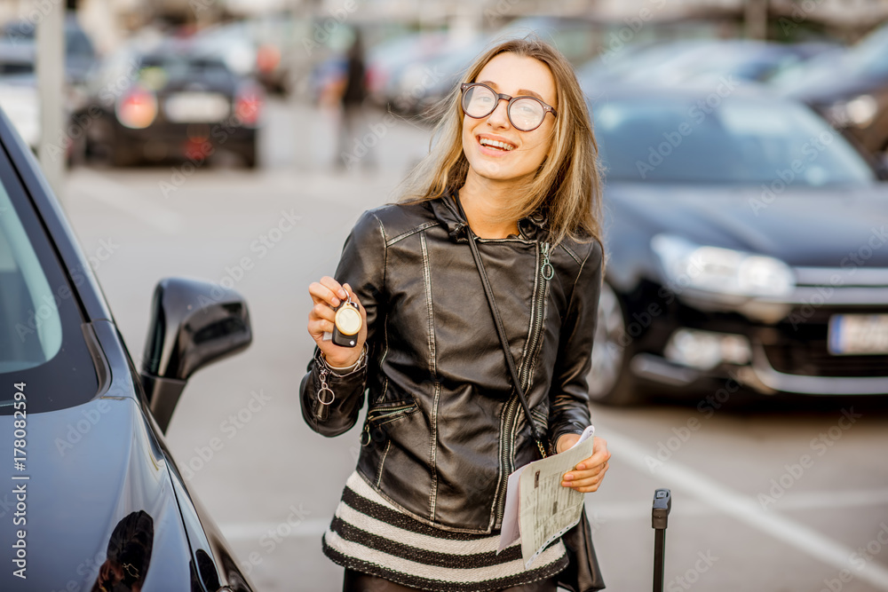 一个年轻快乐的女人的画像，她拿着钥匙和租赁合同，站在户外p上的汽车附近