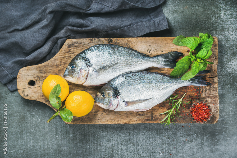 新鲜未煮熟的鲷鱼或多拉多鱼，配柠檬、香草和香料，放在乡村木板上。