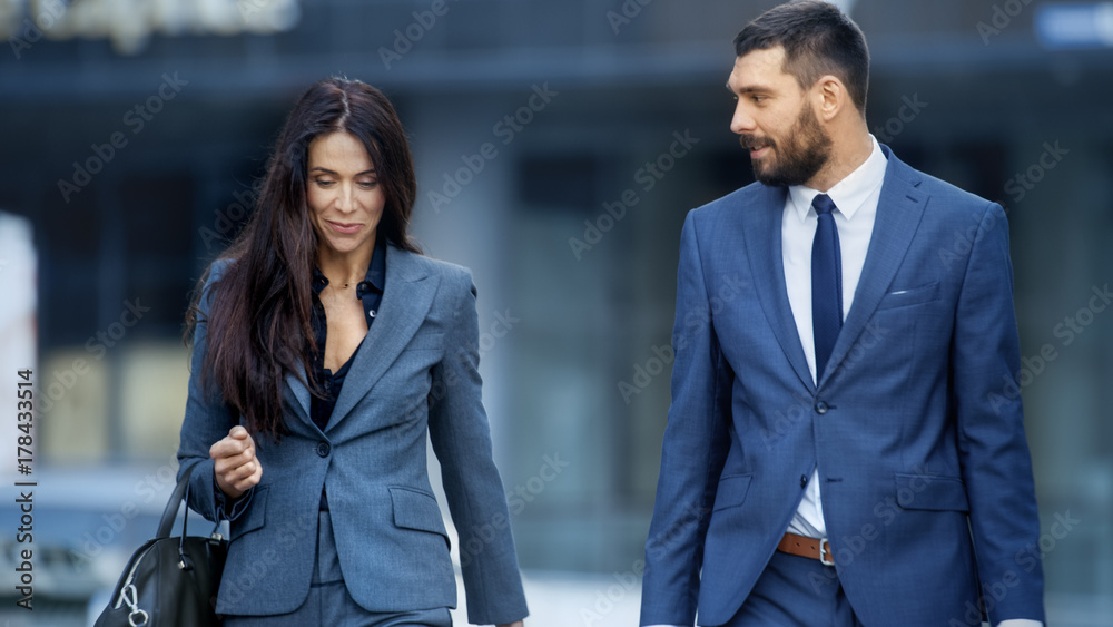 商务女性和商务男性穿着定制西装走在繁忙的大城市街道上。