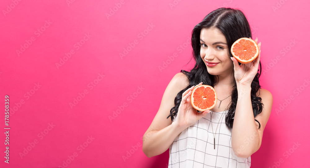 粉红色背景下拿着橘子的快乐年轻女人