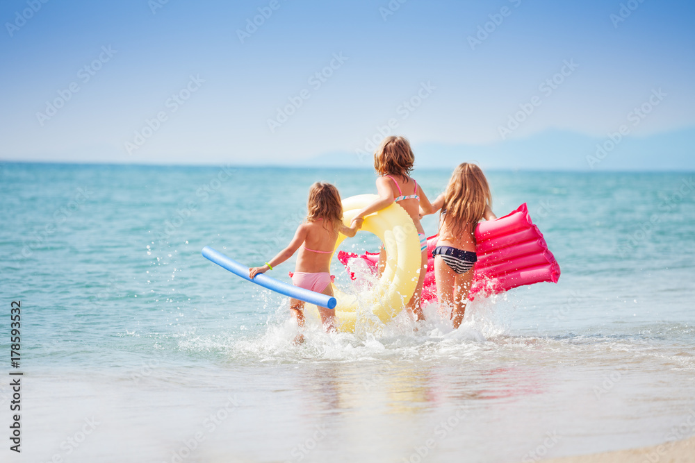 三个女孩拿着游泳工具跑向大海