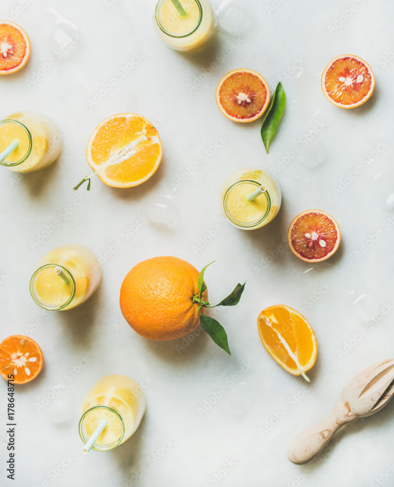健康的黄色奶昔，配柑橘类水果、生姜和冰块，装在浅色大理石台面上