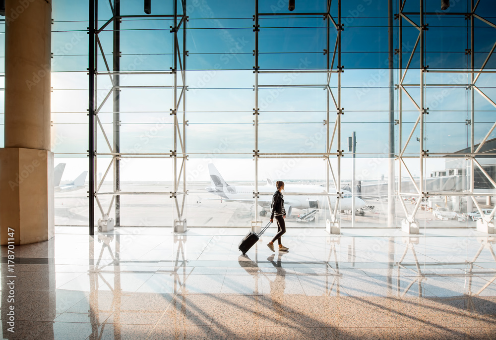 在机场候机厅，一名妇女提着行李箱走在机场的窗户上。寡妇