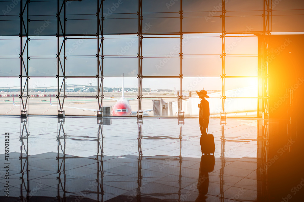 日落时分，在候机大厅，一名妇女提着行李箱走在机场的窗户上。