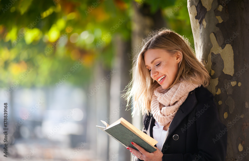 年轻女子在城市街道上五颜六色的秋树下户外看书