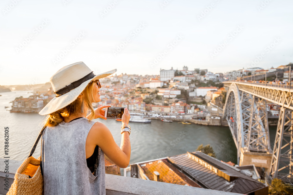 年轻女性游客用手机拍摄河边古镇的美丽风景