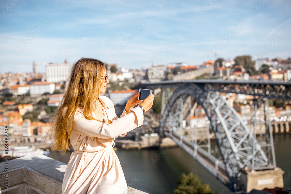 年轻女子用手机拍摄波尔图市著名铁桥的美丽城市景观，