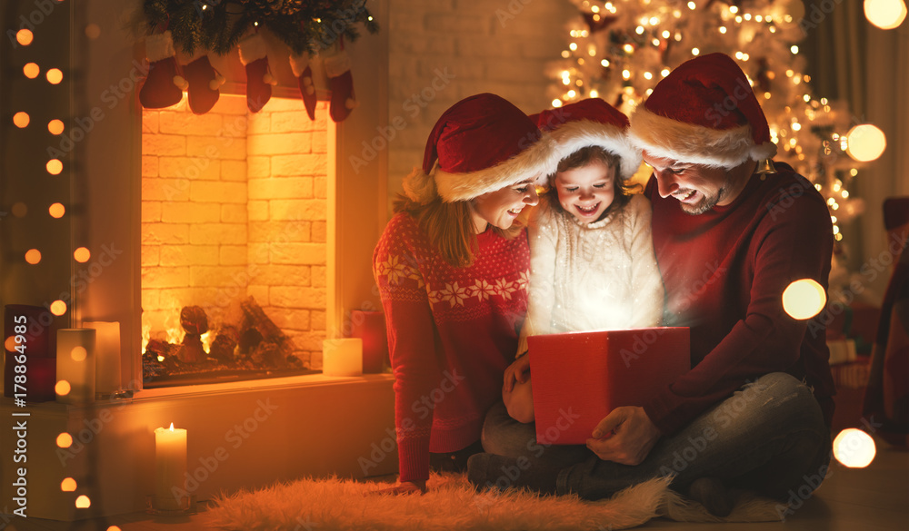 圣诞快乐！幸福的家庭母亲、父亲和孩子在树旁送上魔法礼物