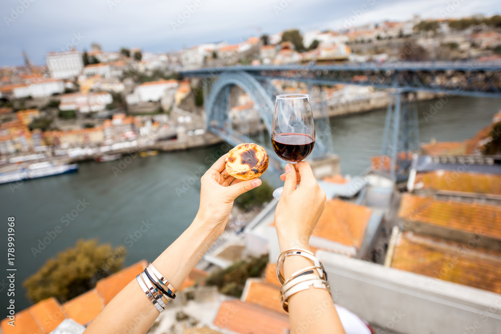 Holding a glass of red wine with traditional portuguese dessert called pastel de Nata on the beautif