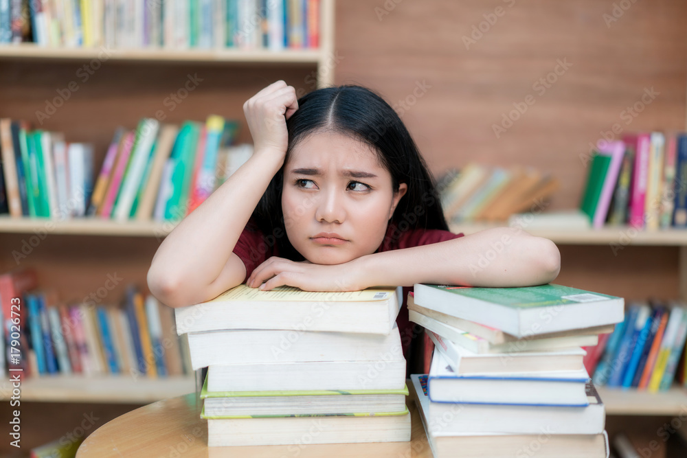 亚洲女学生无聊地在图书馆看书，大学里有很多书。亚洲学生