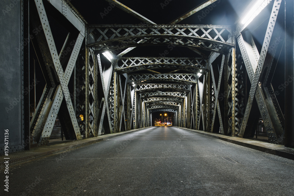 城市桥梁钢结构下的沥青路。汽车灯光下的城市夜景
