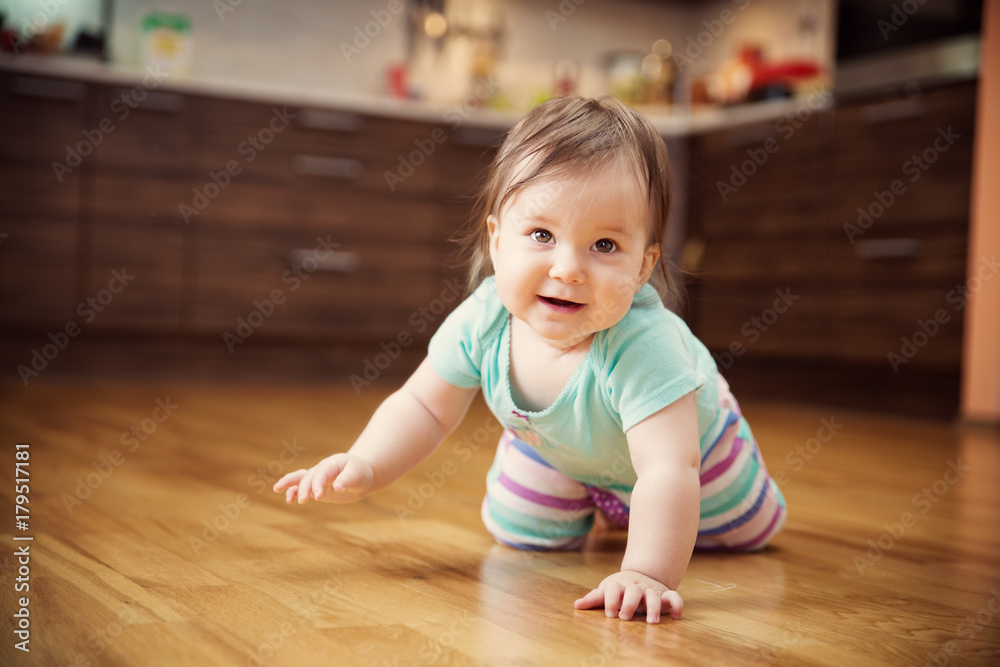 Cute smiling little baby girl crawling on the floor at kitchen. Seven month old infant child at home