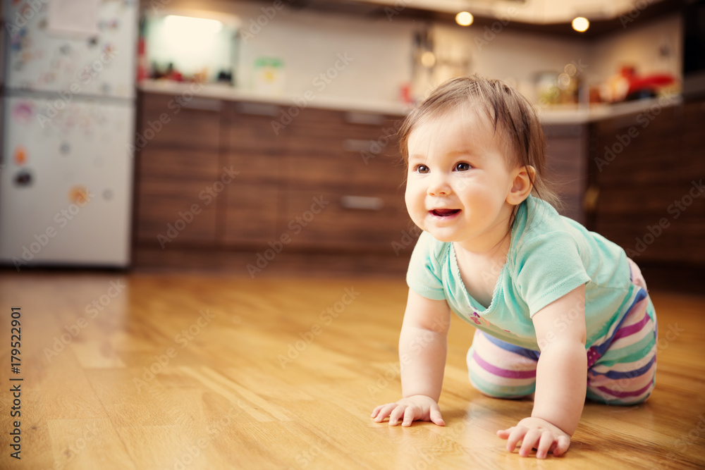 可爱的微笑小女婴在厨房的地板上爬行。家里有七个月大的婴儿