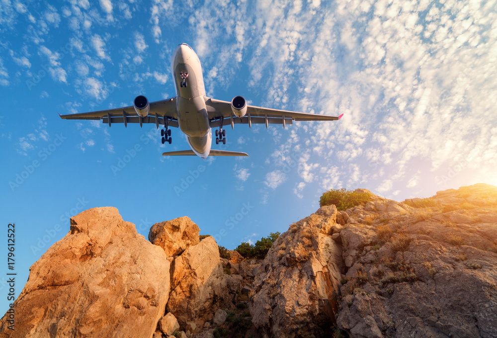 日落时，白色大飞机在岩石上飞行。风景与客机、山脉、山坳融为一体