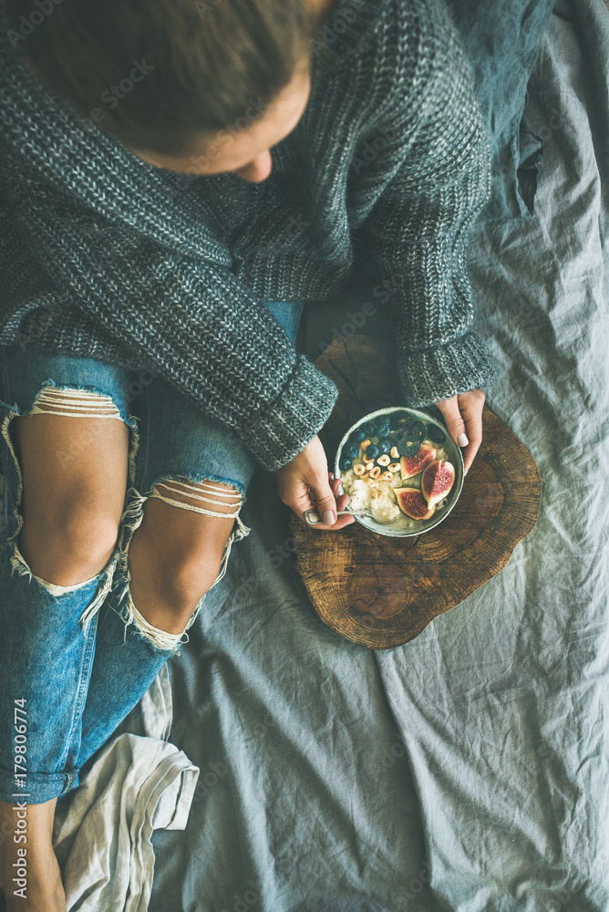 Healthy winter breakfast in bed. Woman in sweater and jeans eating rice coconut porridge with figs, 
