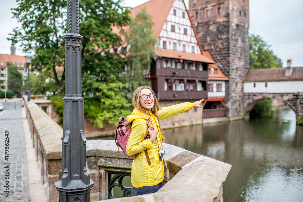 身穿黄色雨衣、背着背包的年轻女游客站在佩尼茨河上的旧桥上