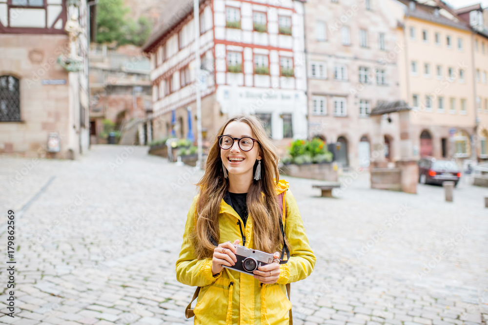 身穿黄色雨衣的年轻女游客背着背包站在身材优美的老广场上
