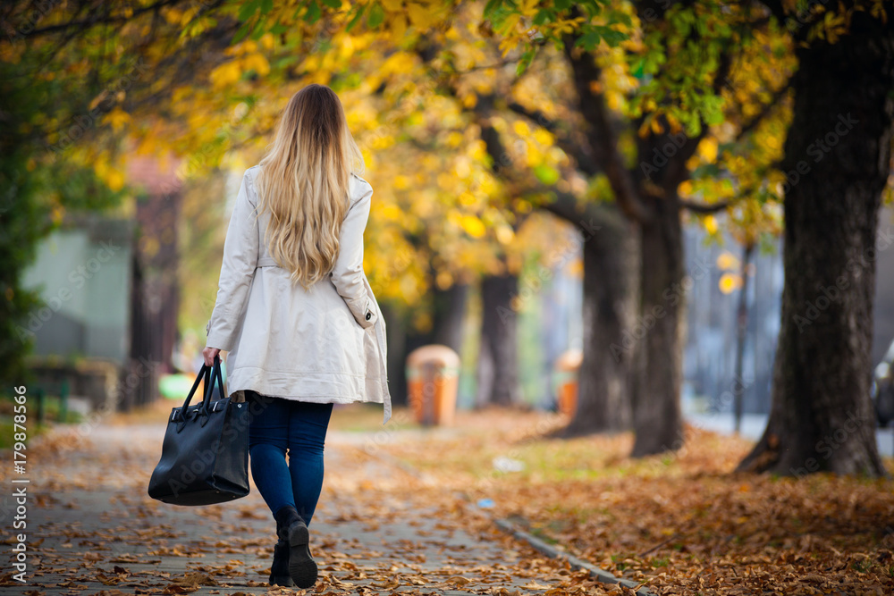 穿着外套的女人走在美丽的秋季城市街道上，后视