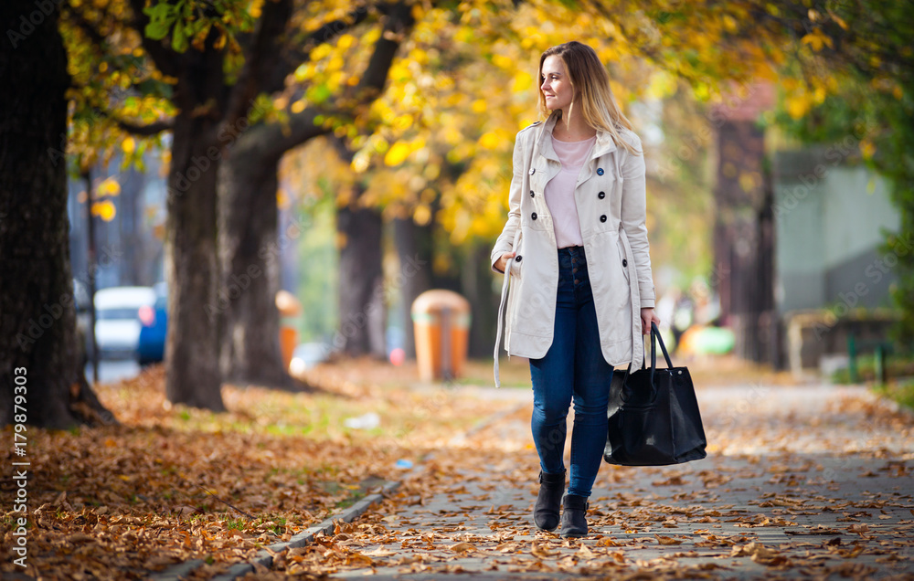 微笑的穿着外套的女人走在美丽的秋日街道上