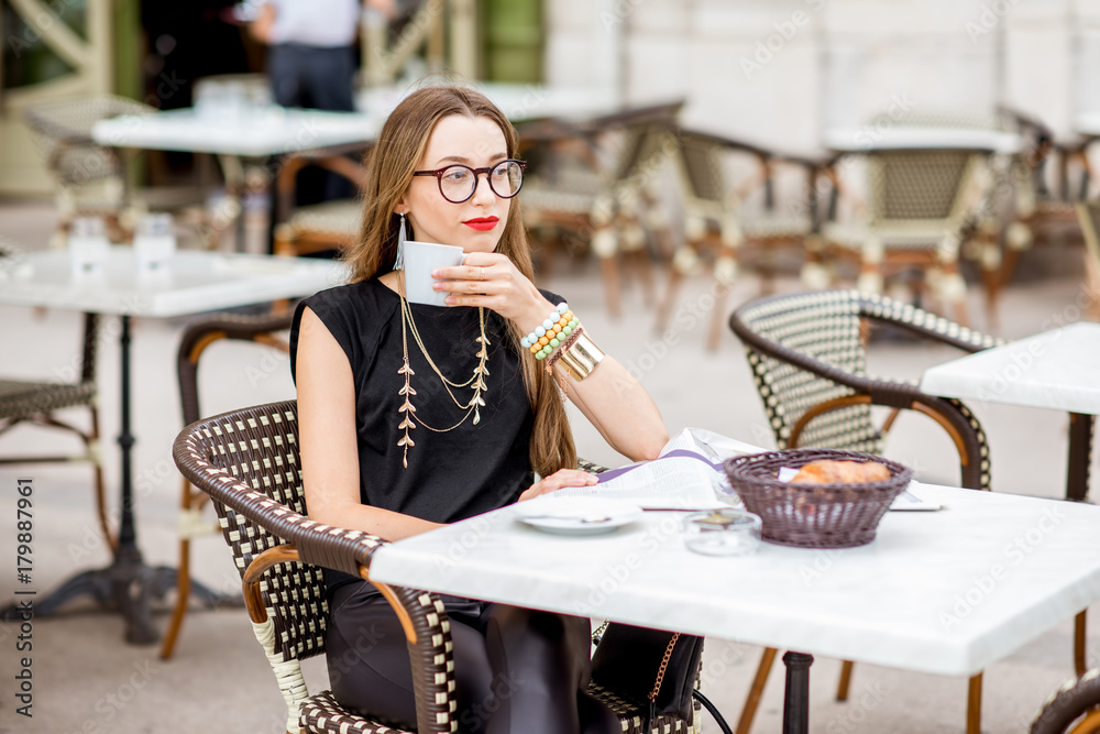 Young woman having a breakfast with coffee and croissant sitting outdoors at the typical french cafe