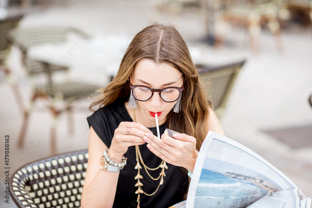年轻女子在户外典型的法式咖啡馆露台上吃早餐时抽烟