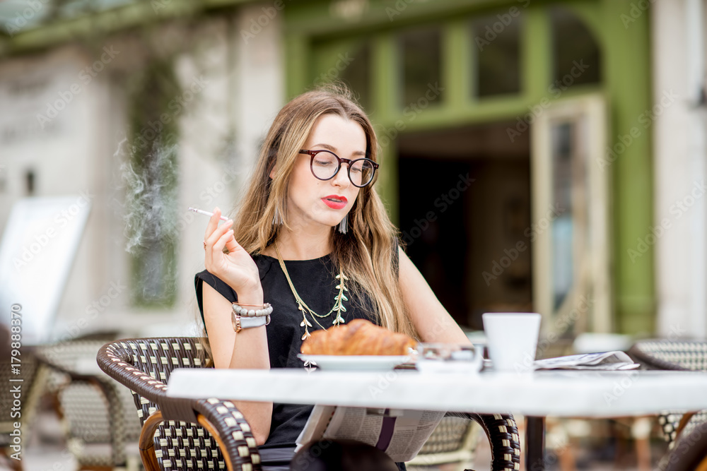 Young woman smoking a cigarette while having a breakfast outdoors at the typical french cafe terrace