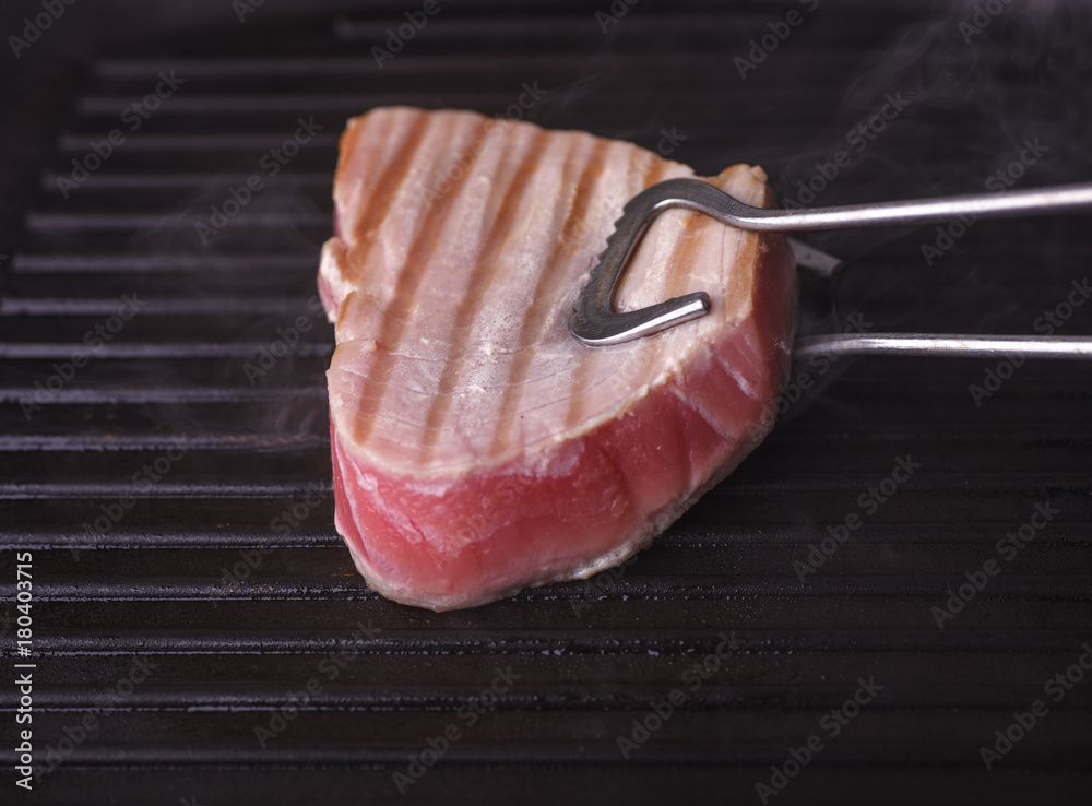 美味的金枪鱼牛排在烤盘上用厨师钳子煎