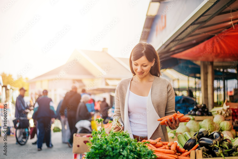 年轻女子在市场上买蔬菜。