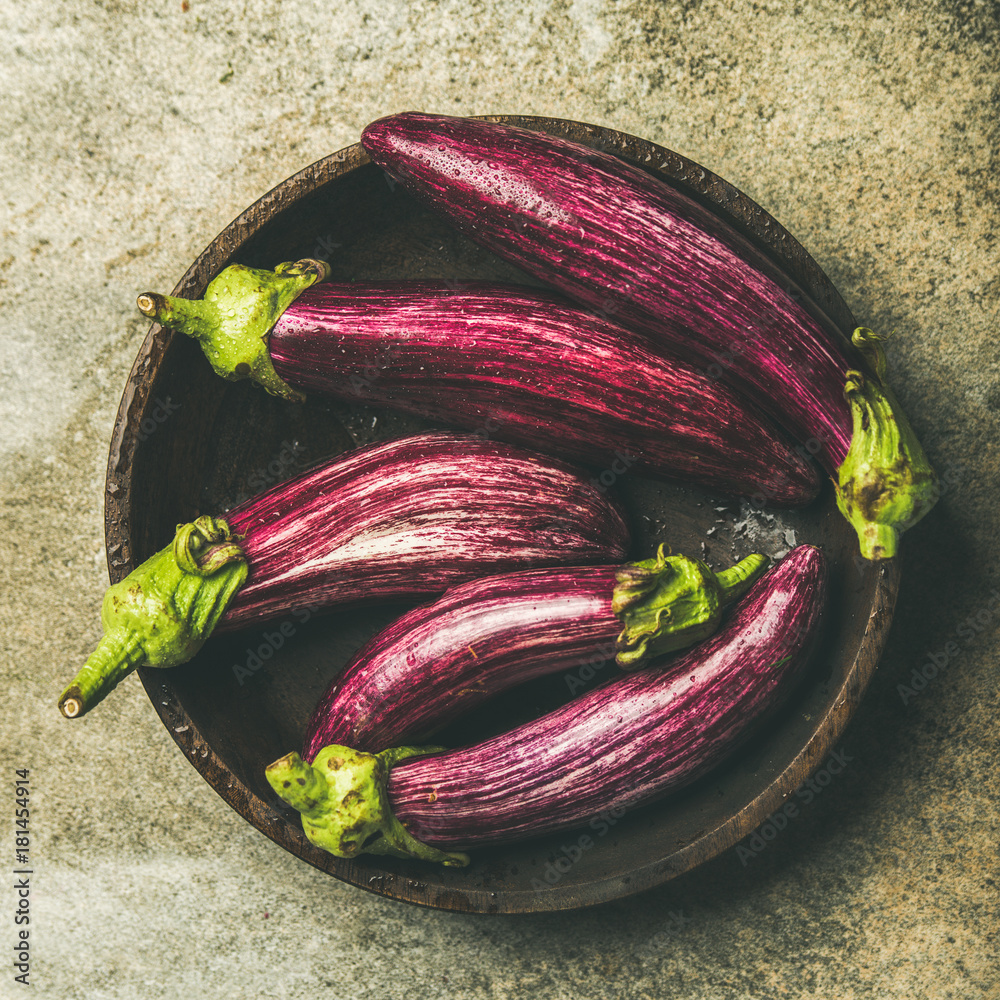 将新鲜的秋季收获的紫色茄子或茄子平放在混凝土石上的木碗中
