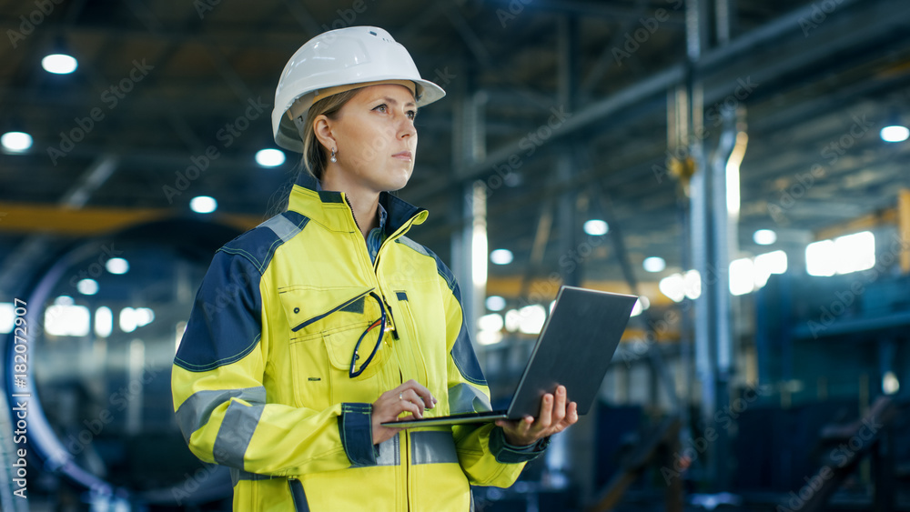 戴着安全帽的女工业工程师在重工业中使用笔记本电脑
