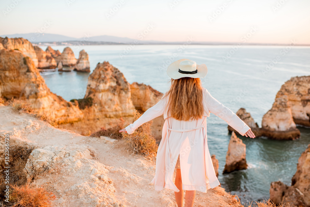 Woman enjoying great view on the rocky coastline during the sunrise in Lagos on the south of Portuga