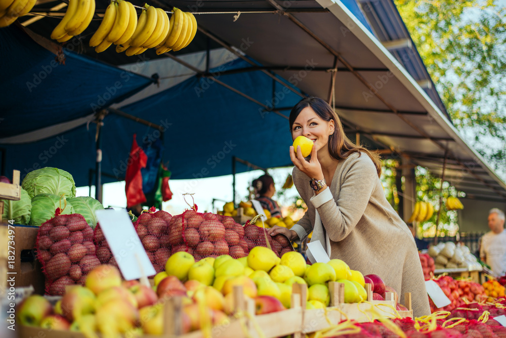 一个女人在市场的货架上买水果，她正在检查苹果。