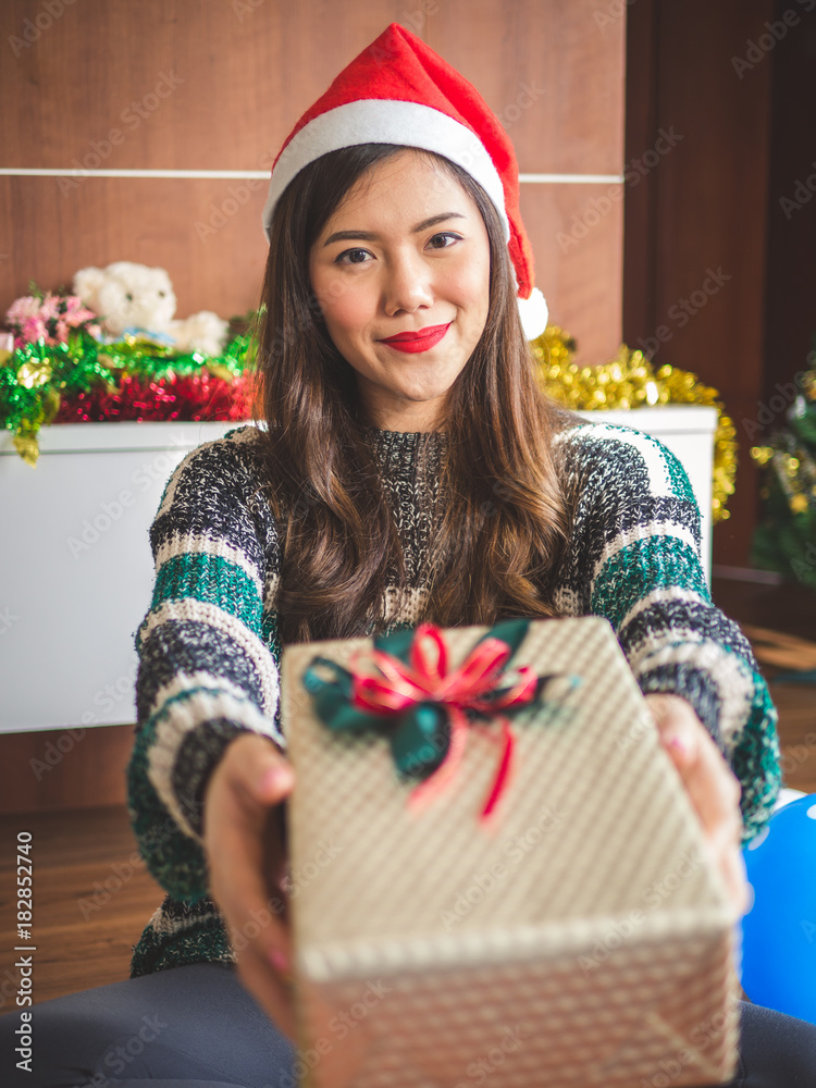 年轻快乐的亚洲女人，戴着圣诞老人帽，手里拿着圣诞派对和庆祝活动的礼盒礼物，