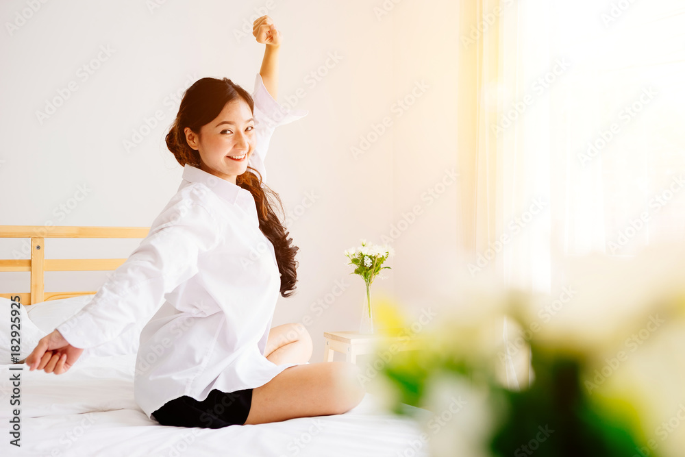 亚洲女性在明亮的早晨醒来。她在白色的床上态度轻松。