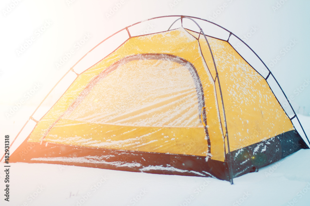一个寒冷的冬日，一顶被雪覆盖的黄色帐篷。雪林中的冬季帐篷营地