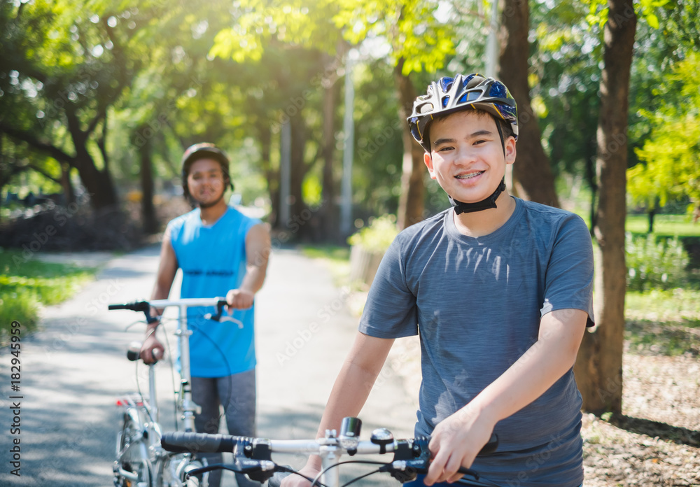 亚洲男孩和朋友夏天在户外绿色公园骑自行车/自行车