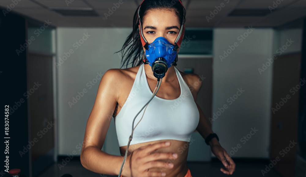 戴着口罩的女运动员在健身房的跑步机上跑步