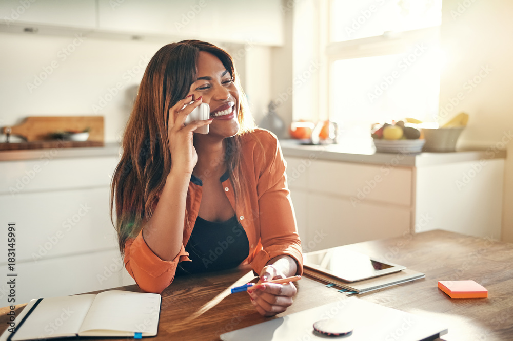 Smiling female entrepreneur talking on a cellphone in her kitche