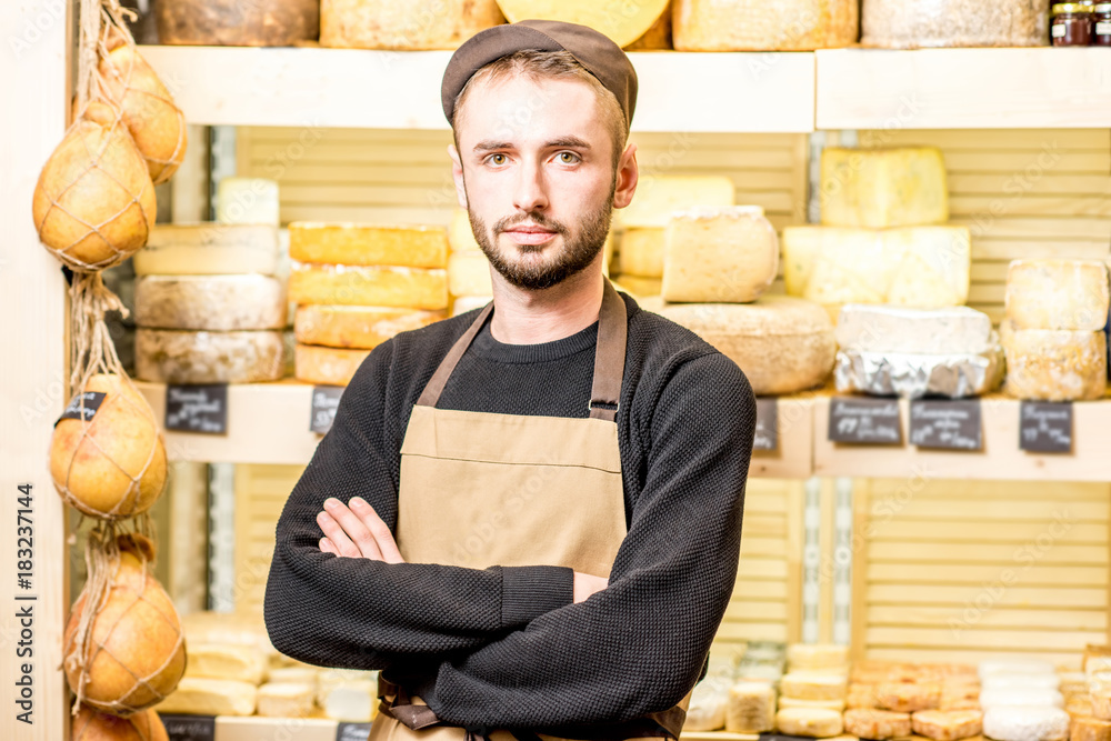 Portrait of a handsome cheese seller in uniform standing in front of the store showcase full of diff
